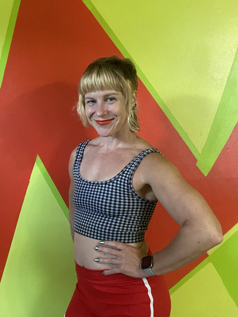 Personal Trainer Jennifer Griswell is posing in front of an orange and green wall